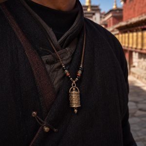 Prayer wheel pendant necklace worn over dark clothing near a monastery