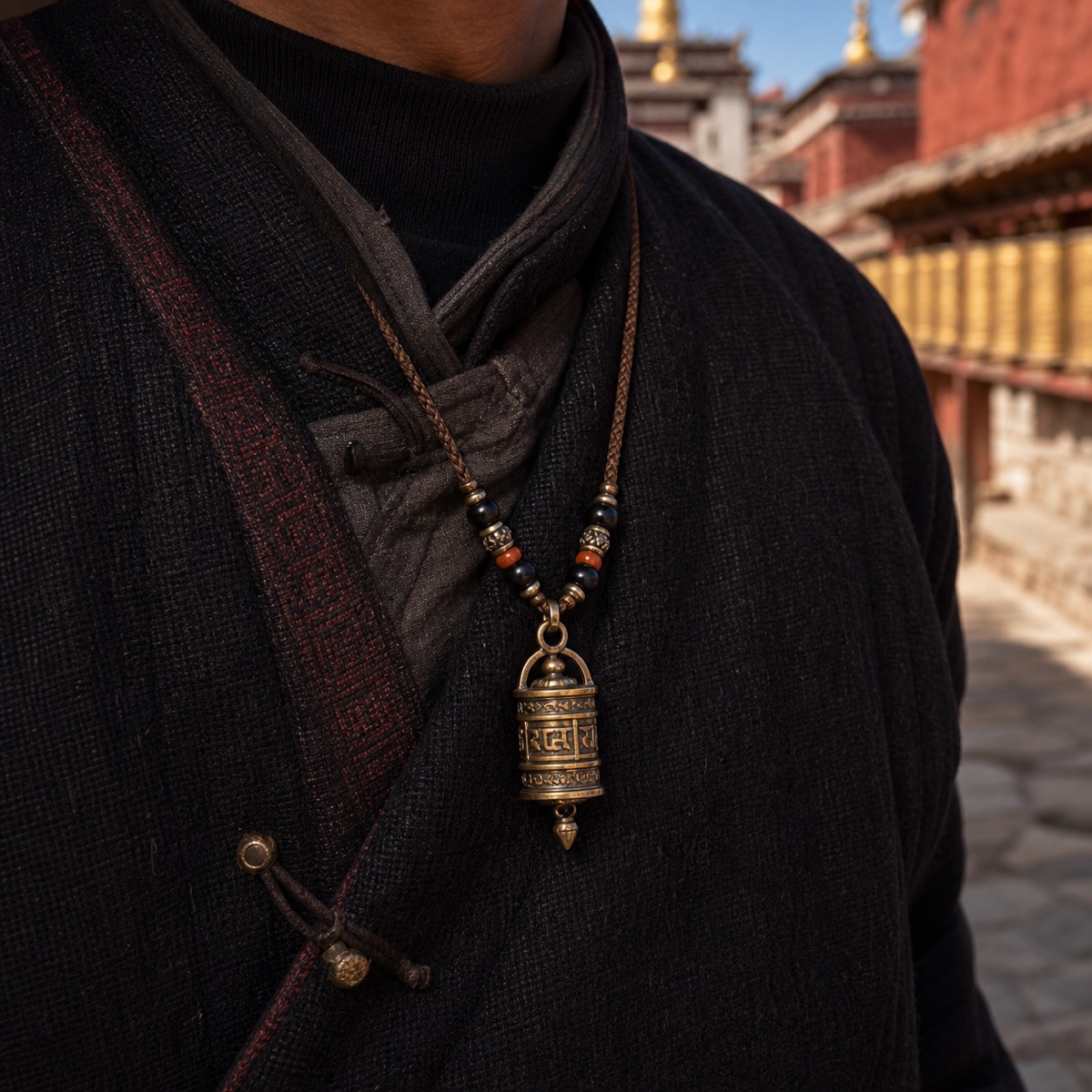 Prayer wheel pendant necklace worn over dark clothing near a monastery